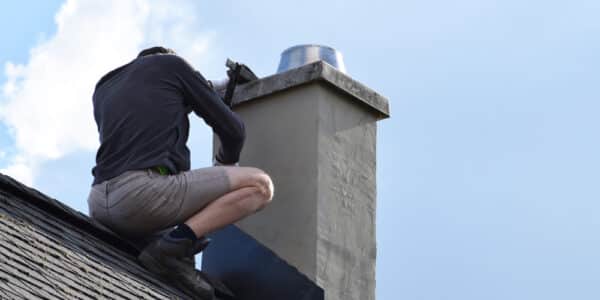 A man repairs the chimney flashing and vent on the roof of a house.